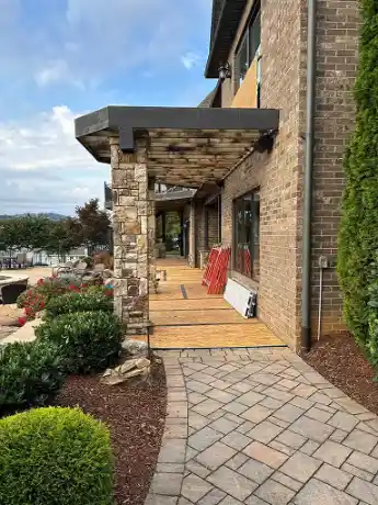 Building's patio under construction with plywood floor and brick pillar beside a landscaped garden path.