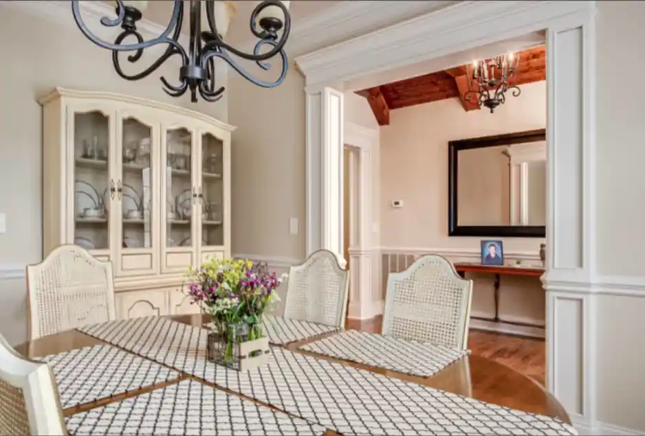 Dining room with wooden table, white chairs, floral centerpiece, glass cabinet, and chandelier light.