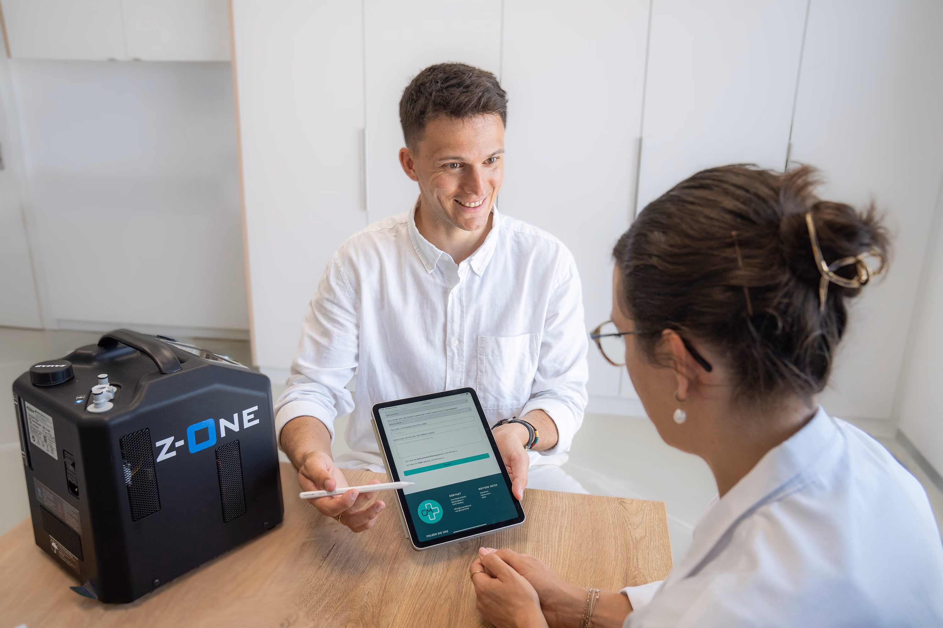Mann zeigt Frau ein Tablet mit Formular, neben ihm steht ein schwarzes Gerät mit Aufschrift Z-ONE.