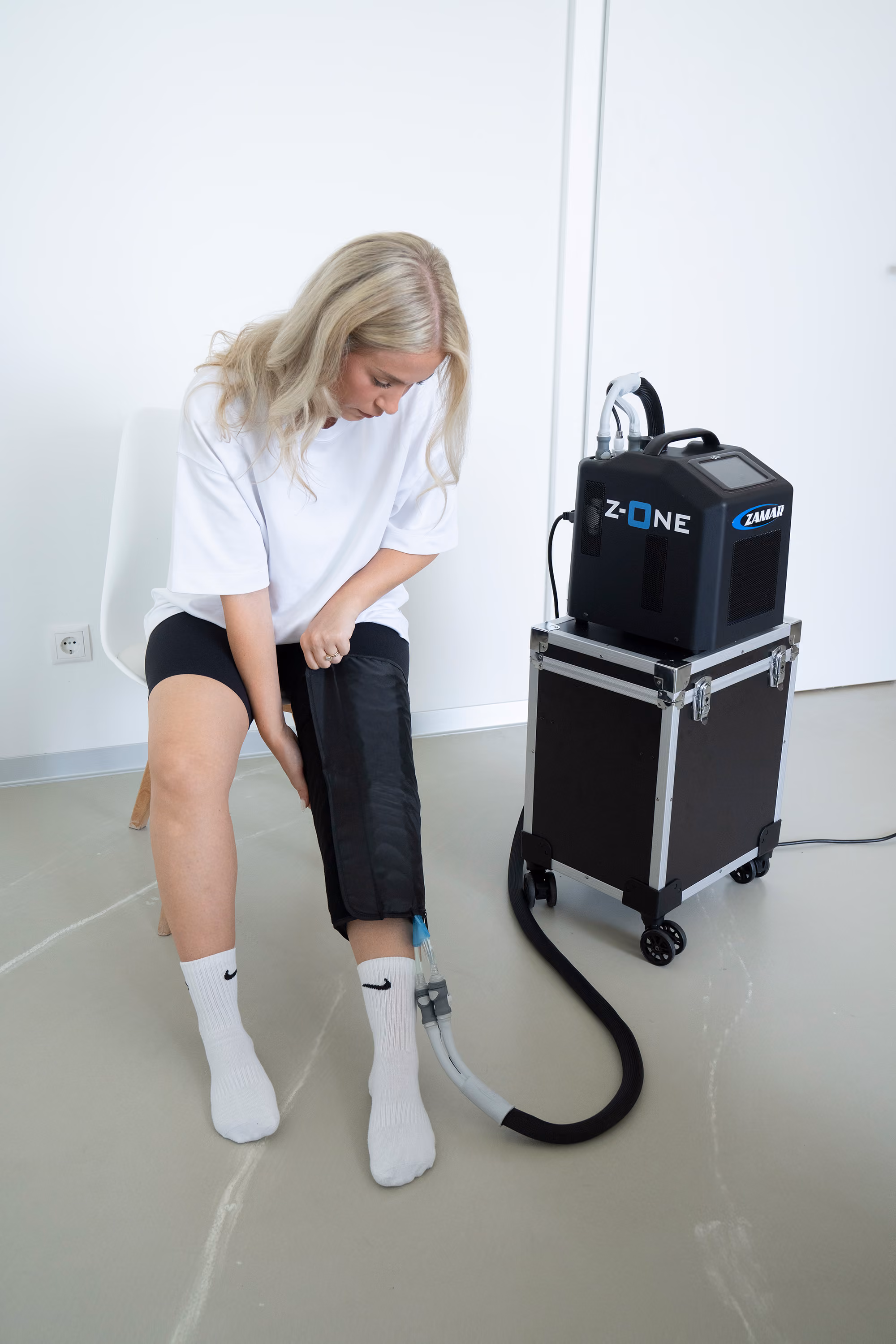 Frau mit weißem T-Shirt und schwarzen Shorts verwendet Z-ONE-Gerät zur Kryotherapie am Bein.