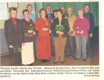Neun Menschen in Reihen, einige halten Blumen, Gruppenfoto bei Vereinswechsel.