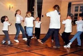 Kinder tanzen gemeinsam in einem Raum mit Holzboden und weißen Wänden.