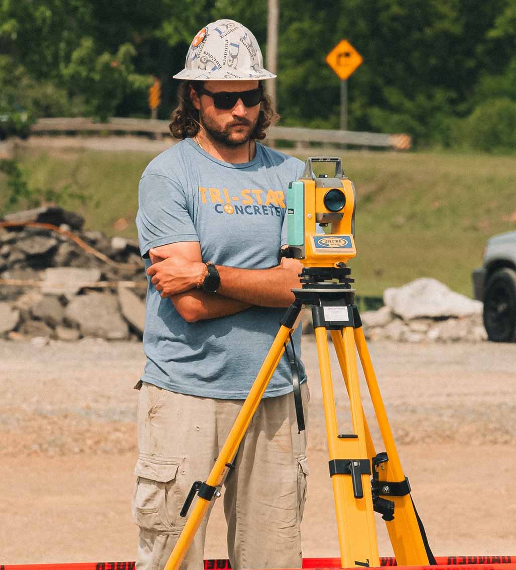Construction worker in hard hat holds surveying equipment on a job site for Tri-Star Concrete.