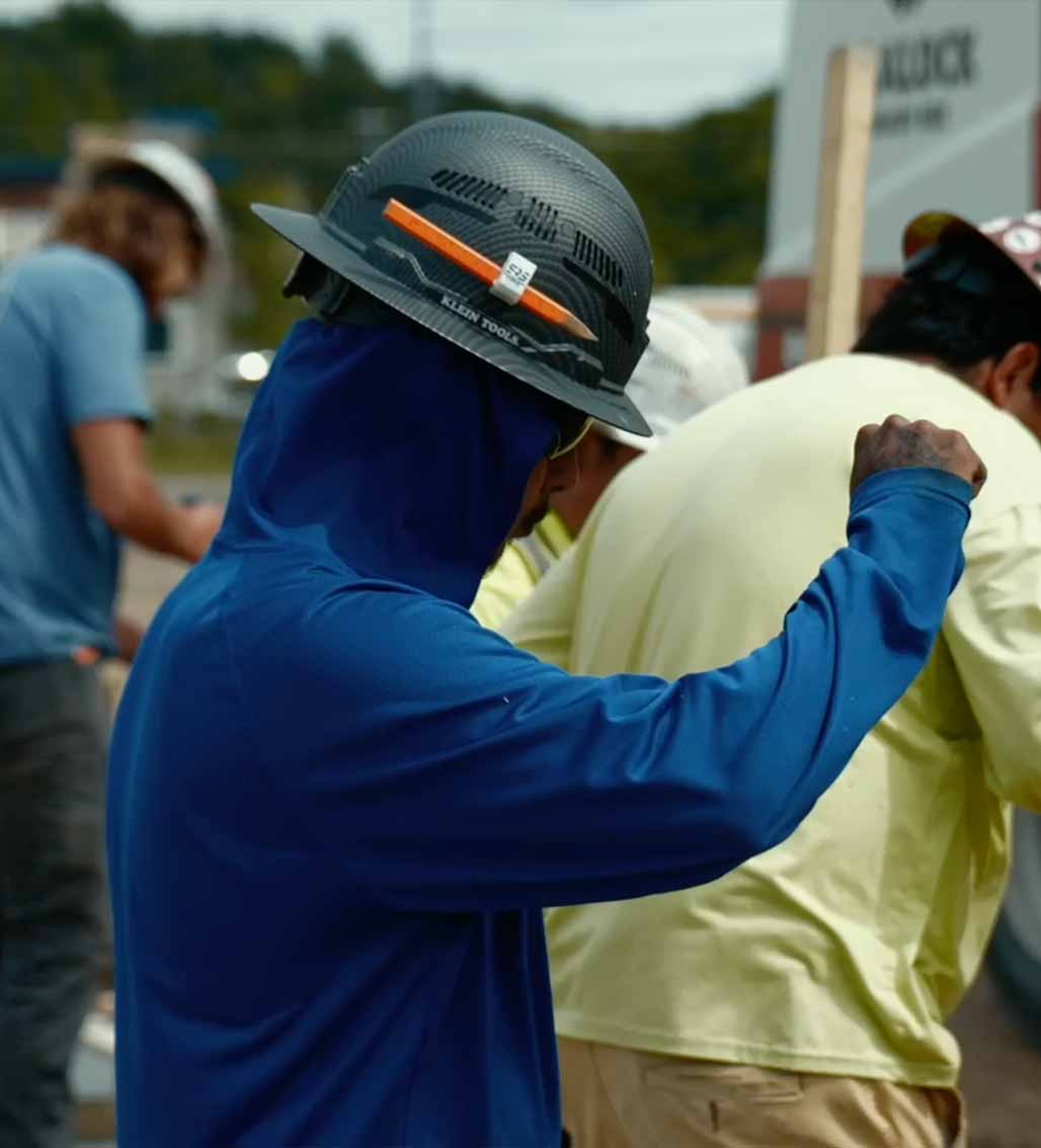 Worker in blue hood and hard hat watches activity on a construction site.