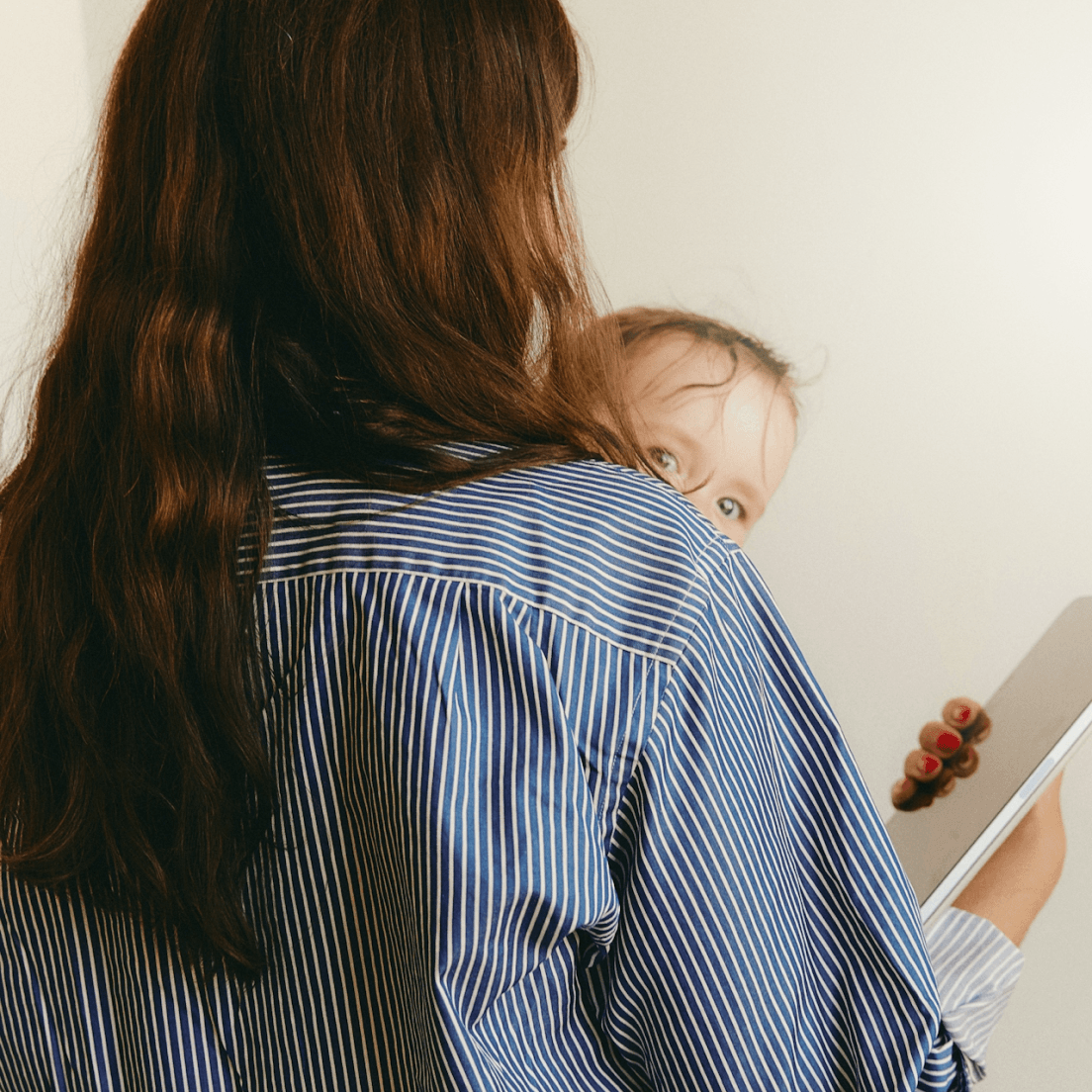 Parent holding a child while using a tablet, representing convenient access to care from home