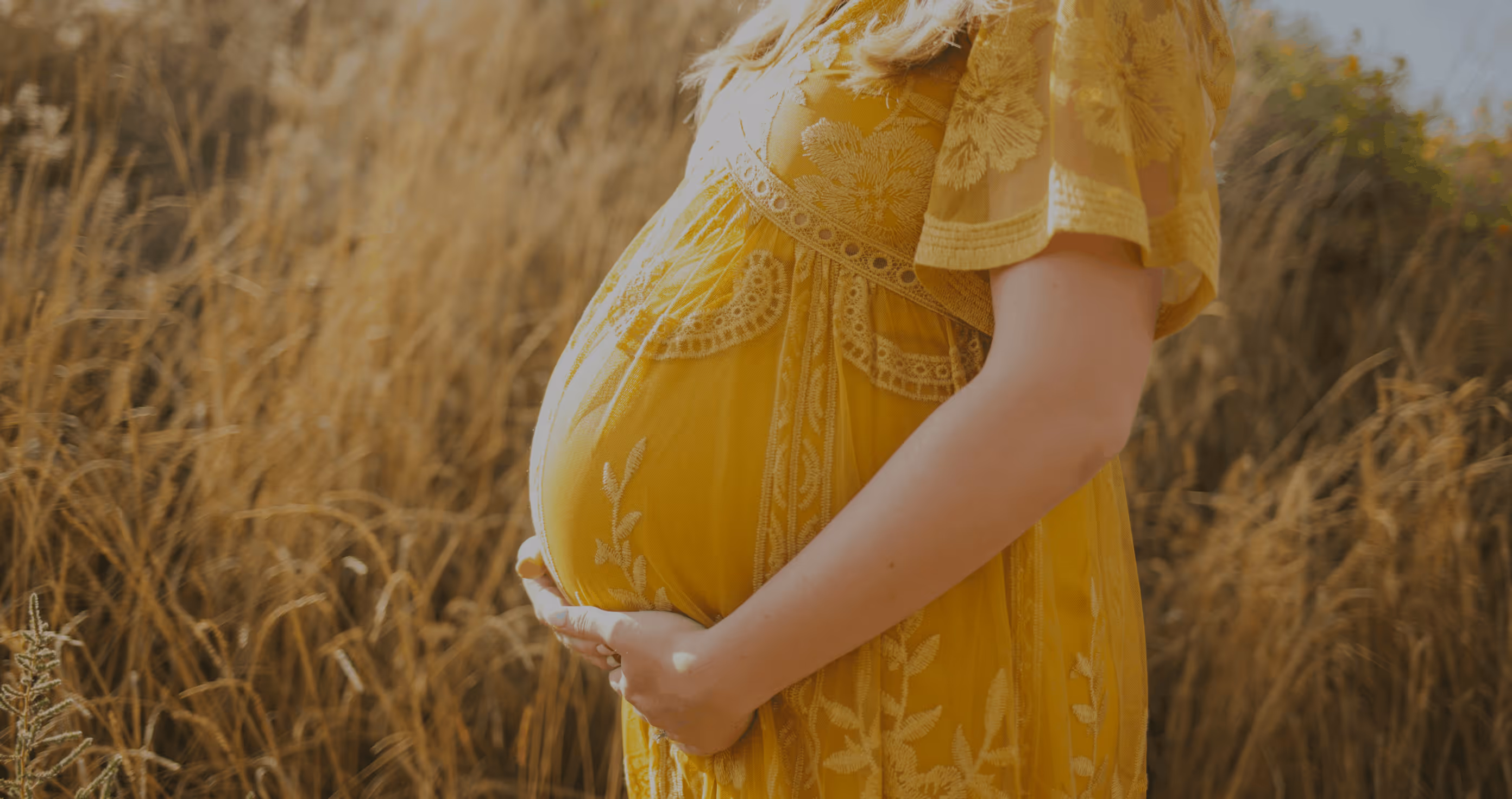 Pregnant woman standing in a field with hands on her belly