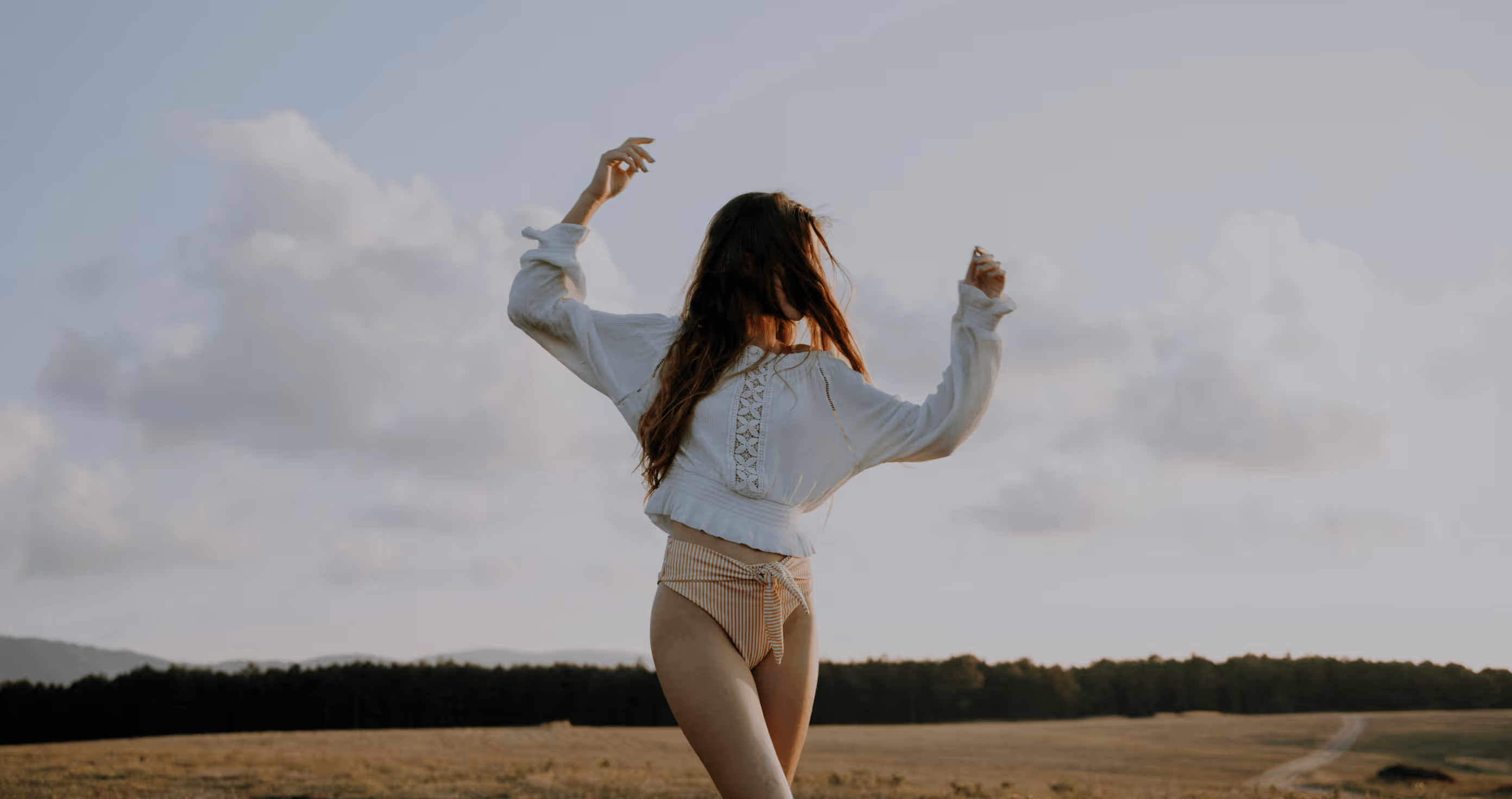 Woman standing outdoors with her arms raised beneath a cloudy sky