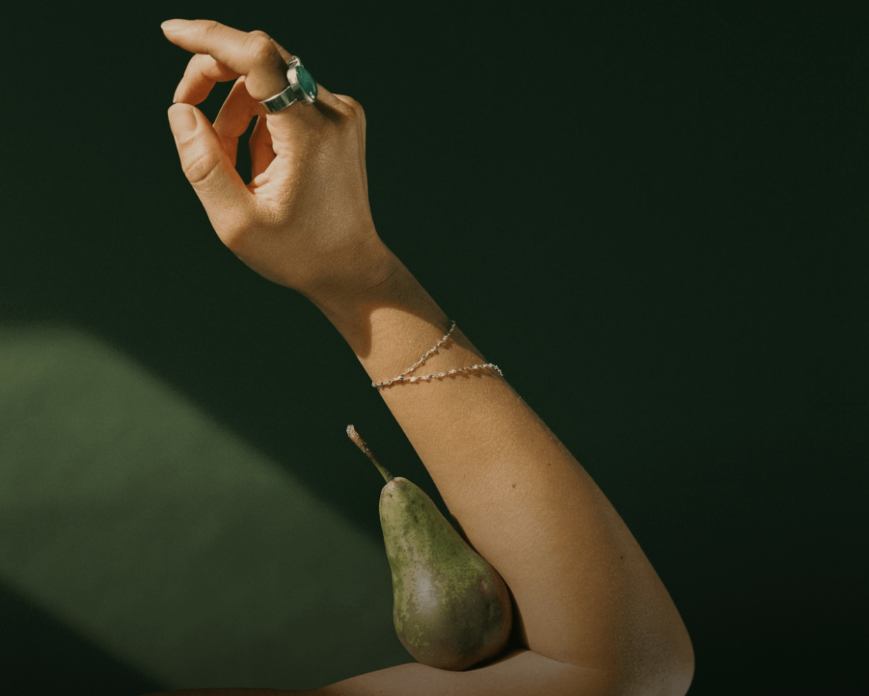 Hand holding a pear reaching upward against a dark background