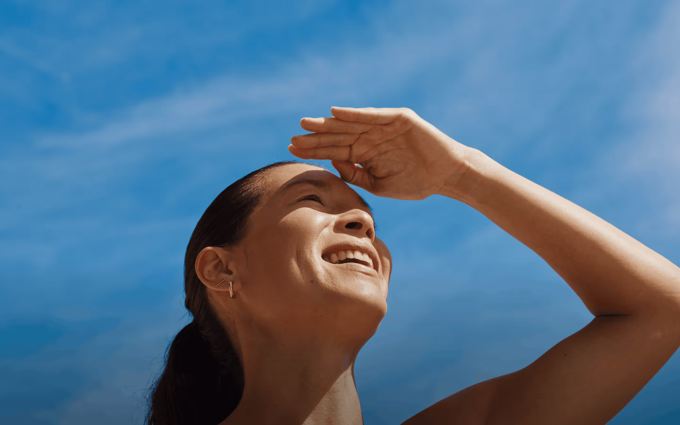 Person smiling outdoors beneath a blue sky