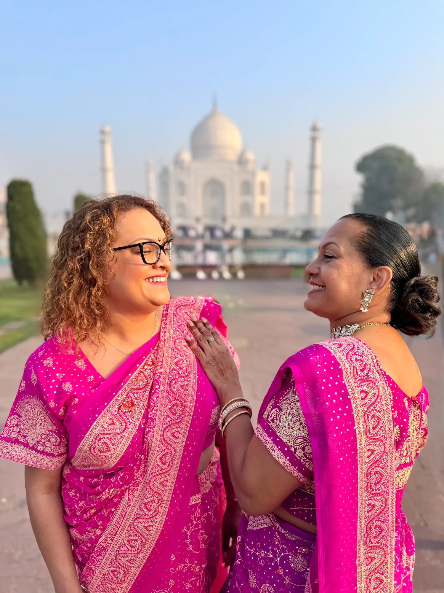 smiling women dressed in pink traditional Indian outfits looking at each other happy at the Taj Mahal
