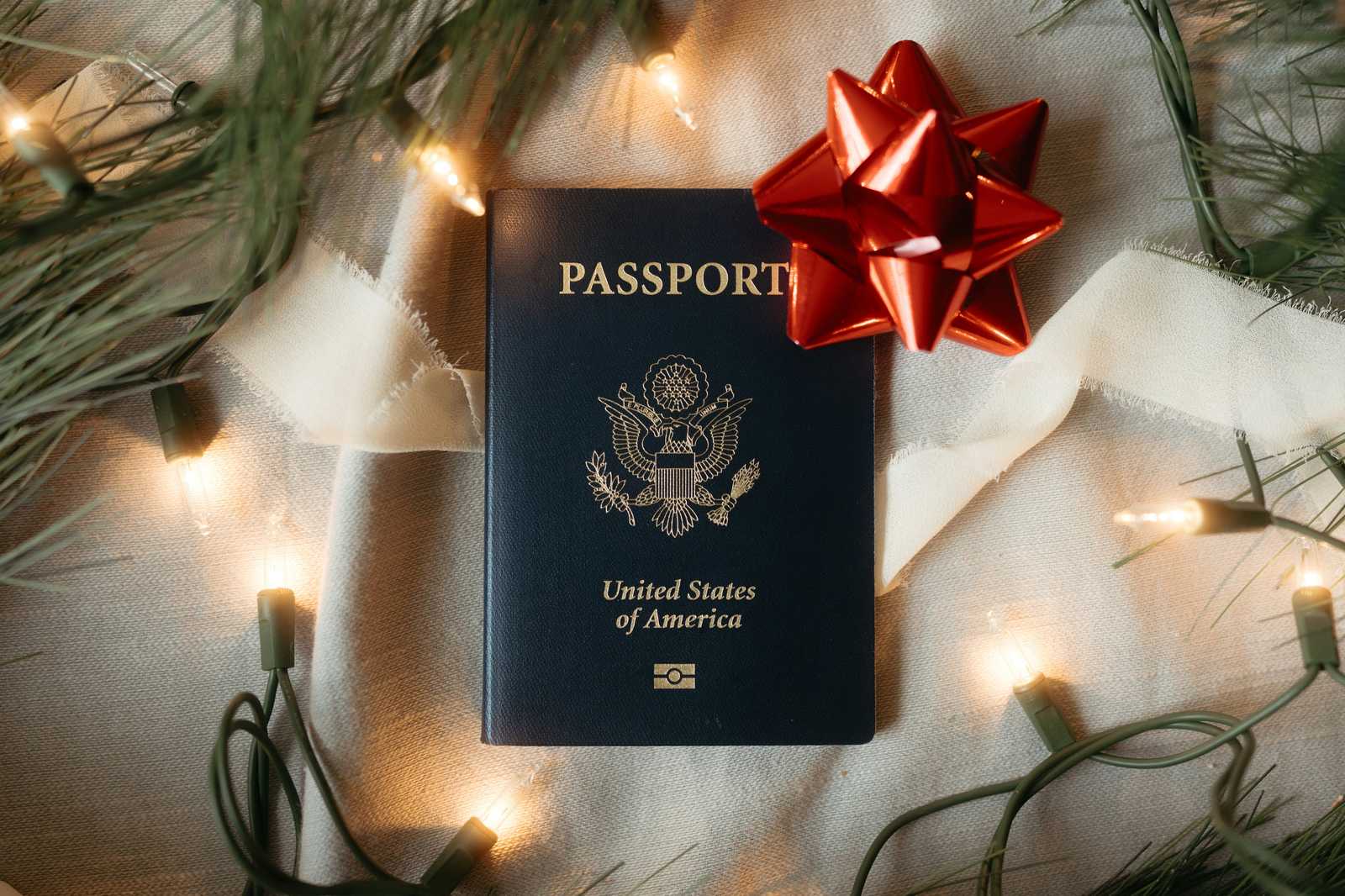 A U.S. passport wrapped with a red gift bow beside holiday lights.