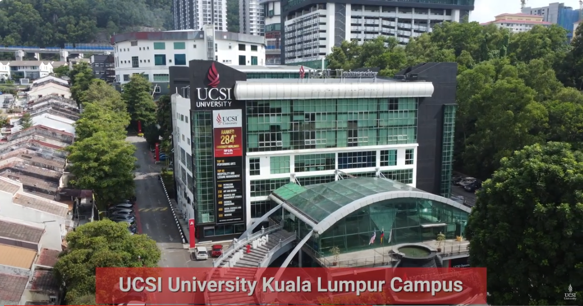 Aerial view of UCSI University Kuala Lumpur Campus showing the main building with its glass entrance and surrounding greenery. The campus banner highlights the university's ranking and programs.