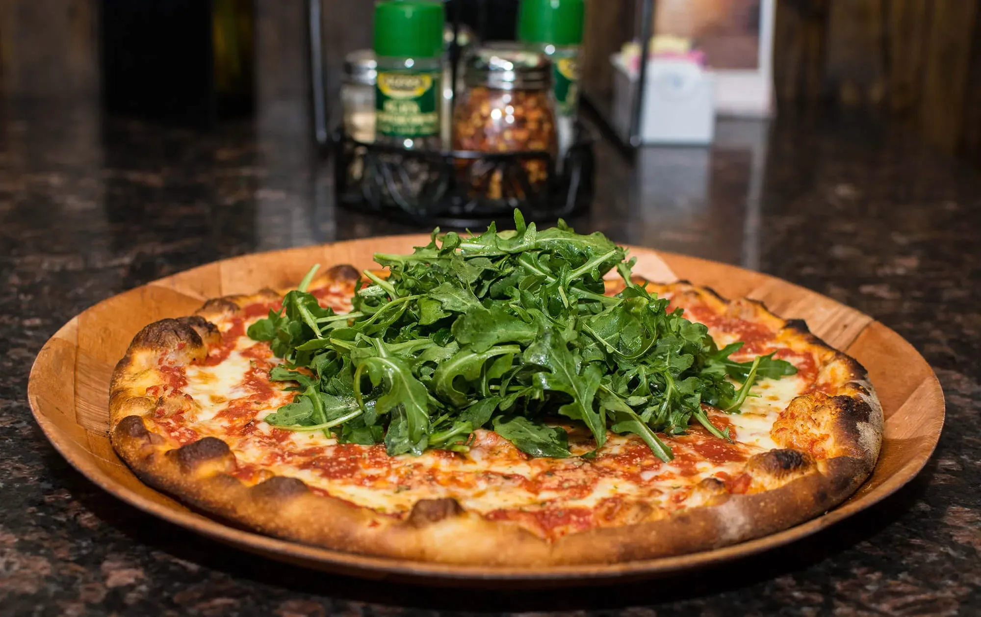 Cheese pizza topped with a large pile of fresh arugula on a wooden plate.