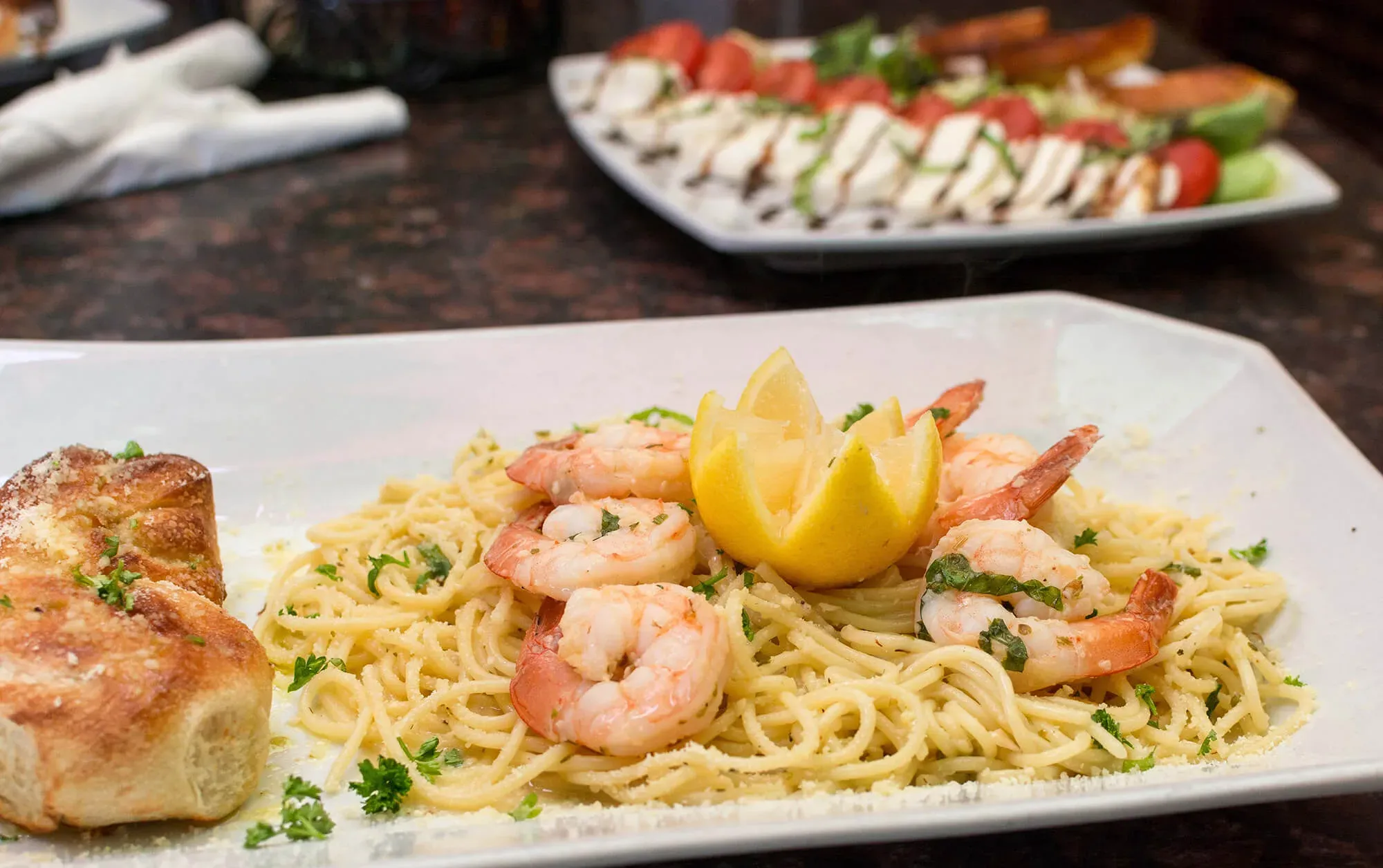 Shrimp scampi pasta with parsley and lemon wedge served with garlic bread on a white plate.