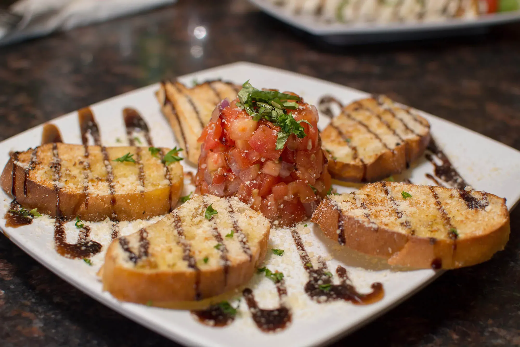 Grilled bread slices arranged around a mound of tomato bruschetta with basil and balsamic drizzle.