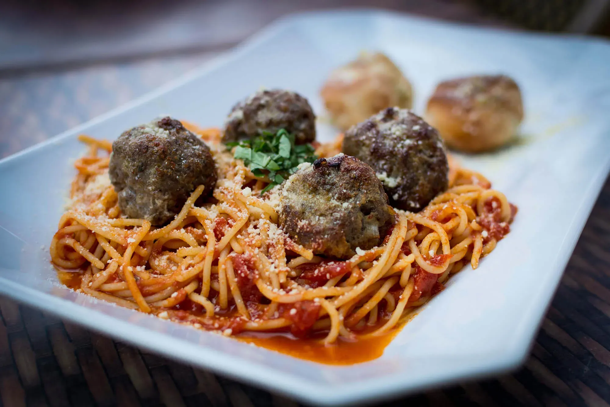 Plate of spaghetti with tomato sauce, meatballs, grated cheese, and garnish on a white dish.