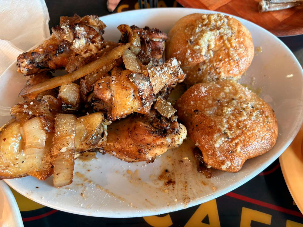 Plate with grilled chicken wings topped with cooked onions and two garlic butter rolls.
