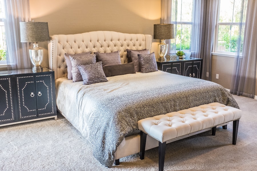 Elegant bedroom with tufted bed, gray pillows, matching lamps, black nightstands, and a cushioned bench.