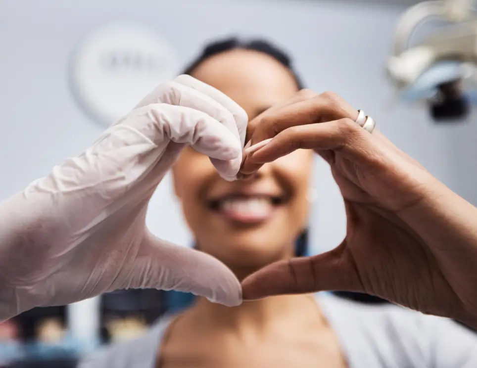 Close-up of a woman and a gloved hand forming a heart shape together. La Perle Dental Center in Edmonton, AB TST 3T9
