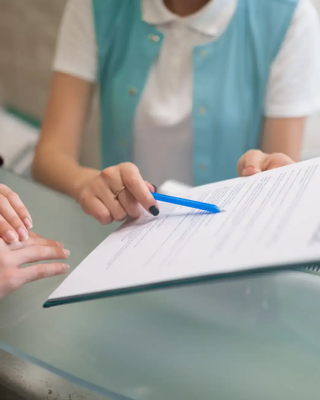 Person pointing at document with blue pen while another person follows along with hands on desk. La Perle Dental Center in Edmonton, AB TST 3T9