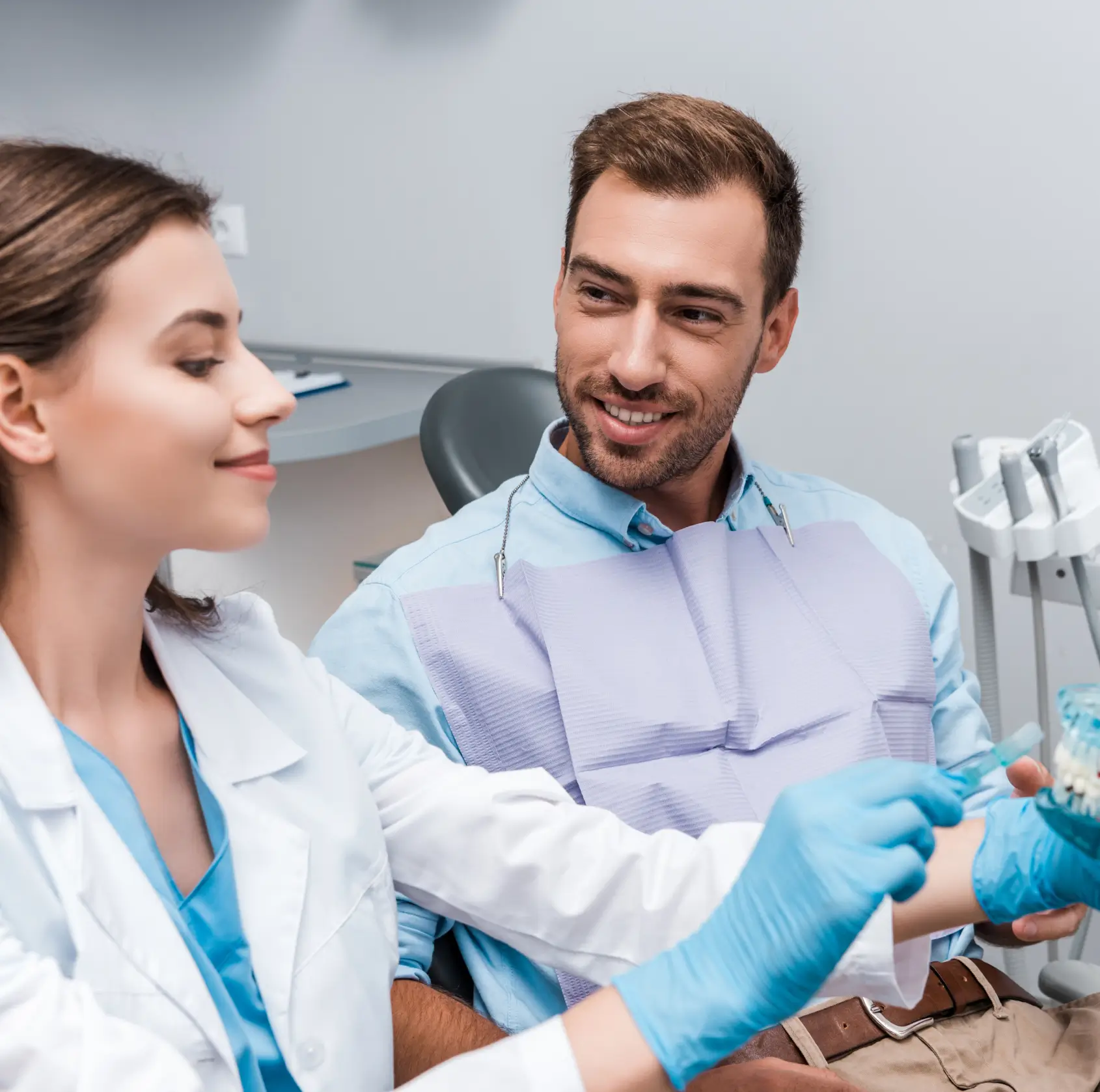 Dentist in gloves showing a dental model to a male patient seated in a clinic chair. La Perle Dental Center in Edmonton, AB TST 3T9