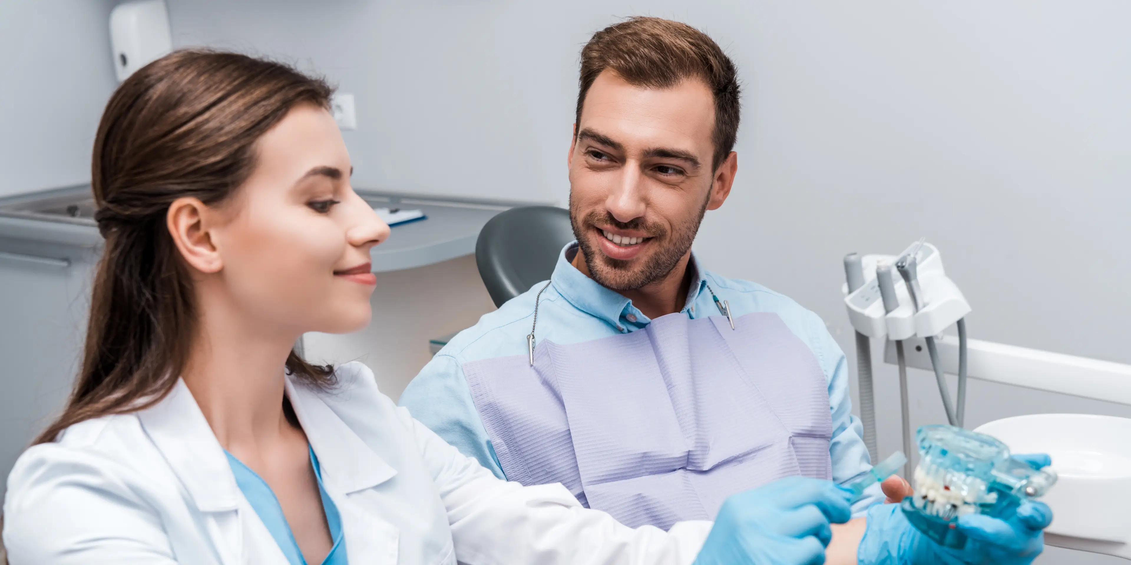 Dentist showing dental model to male patient in clinic with patient wearing a bib. La Perle Dental Center in Edmonton, AB TST 3T9