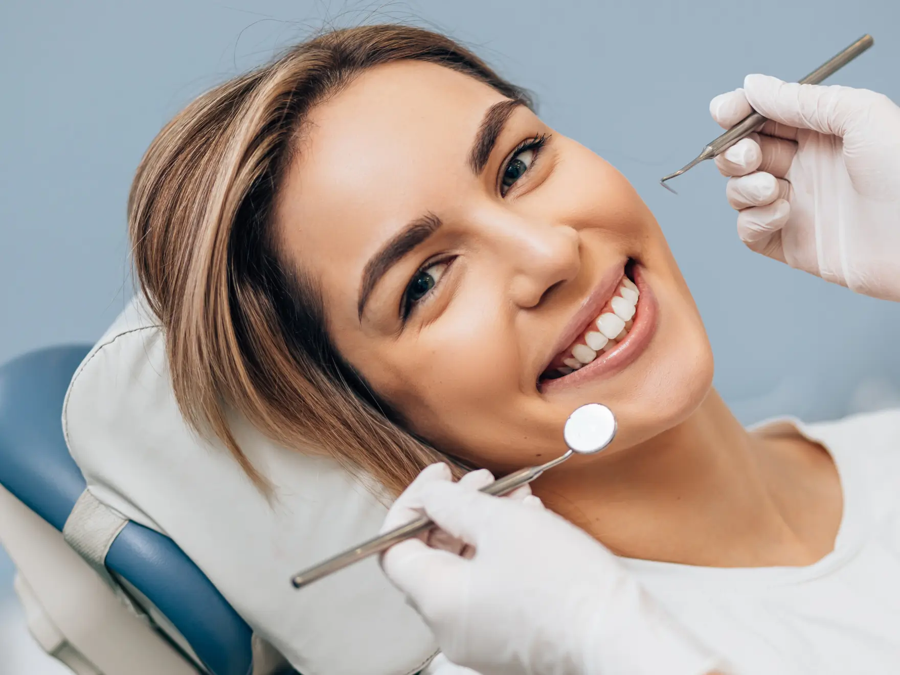 Smiling woman reclined in dental chair during checkup with dentist holding dental tools. La Perle Dental Center in Edmonton, AB TST 3T9