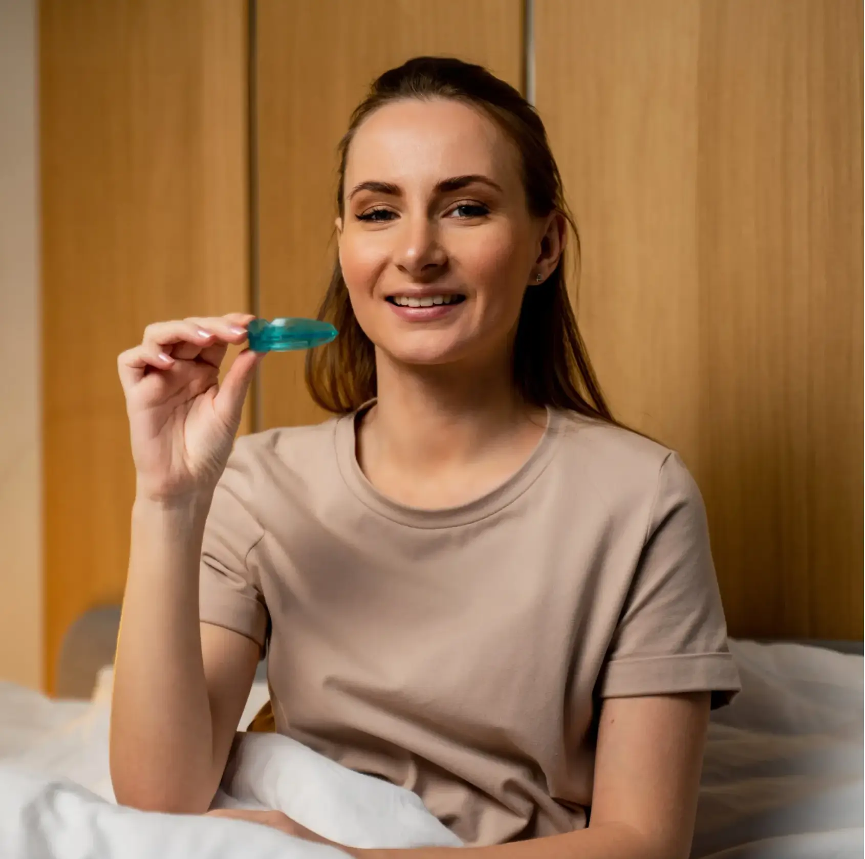 Smiling woman sitting in bed holding a blue mouthguard in her hand. La Perle Dental Center in Edmonton, AB TST 3T9