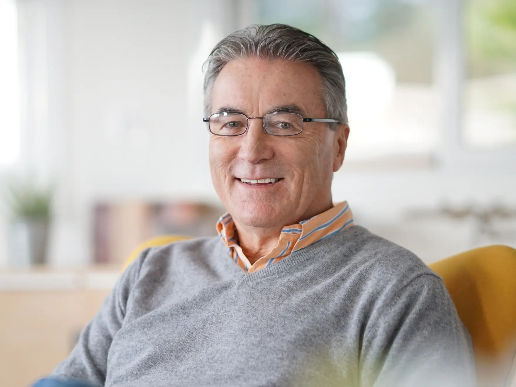 Smiling mature man wearing glasses and a gray sweater sitting in a bright room. La Perle Dental Center in Edmonton, AB TST 3T9