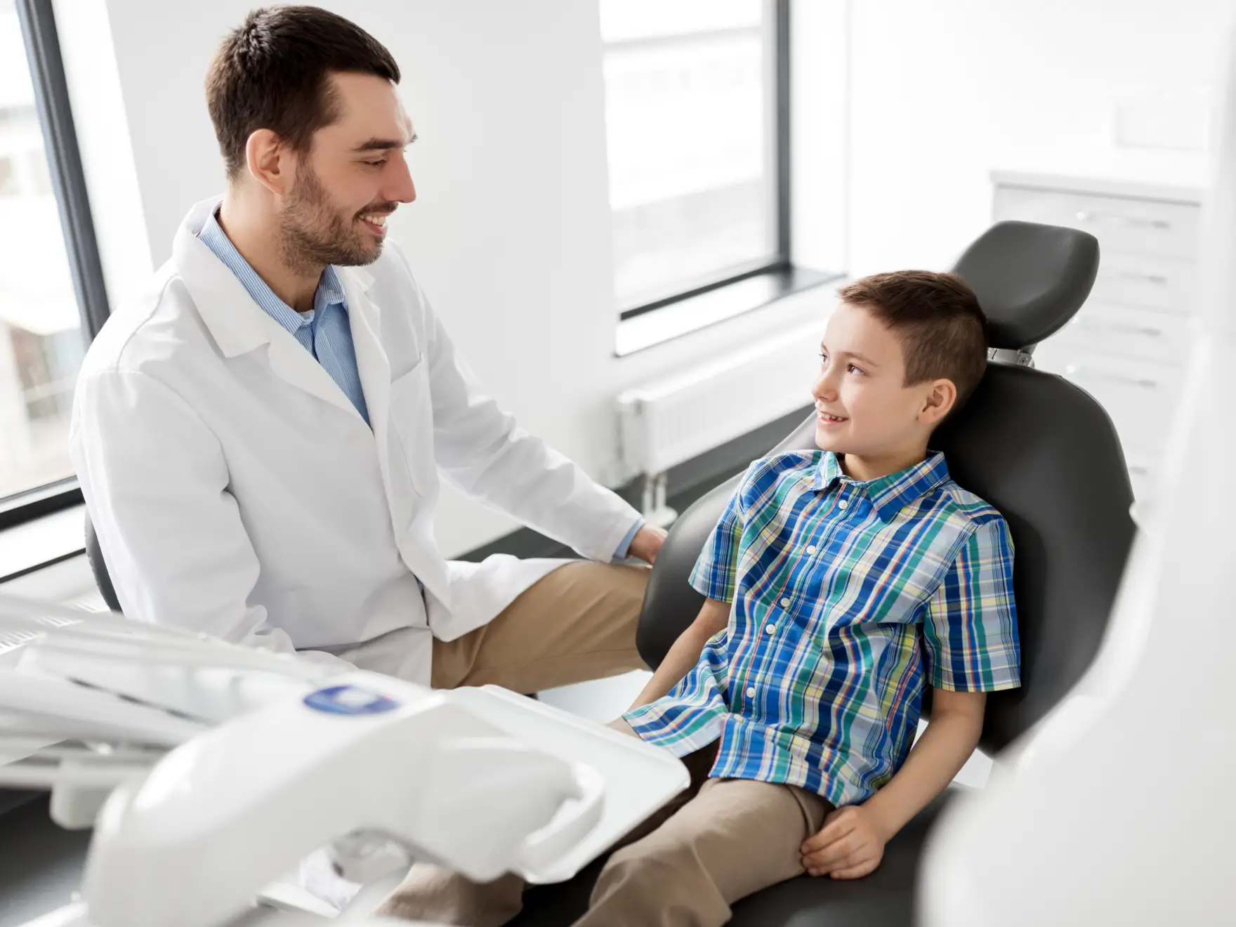 Male dentist in white coat smiling and talking with a boy sitting in a dental chair. La Perle Dental Center in Edmonton, AB TST 3T9