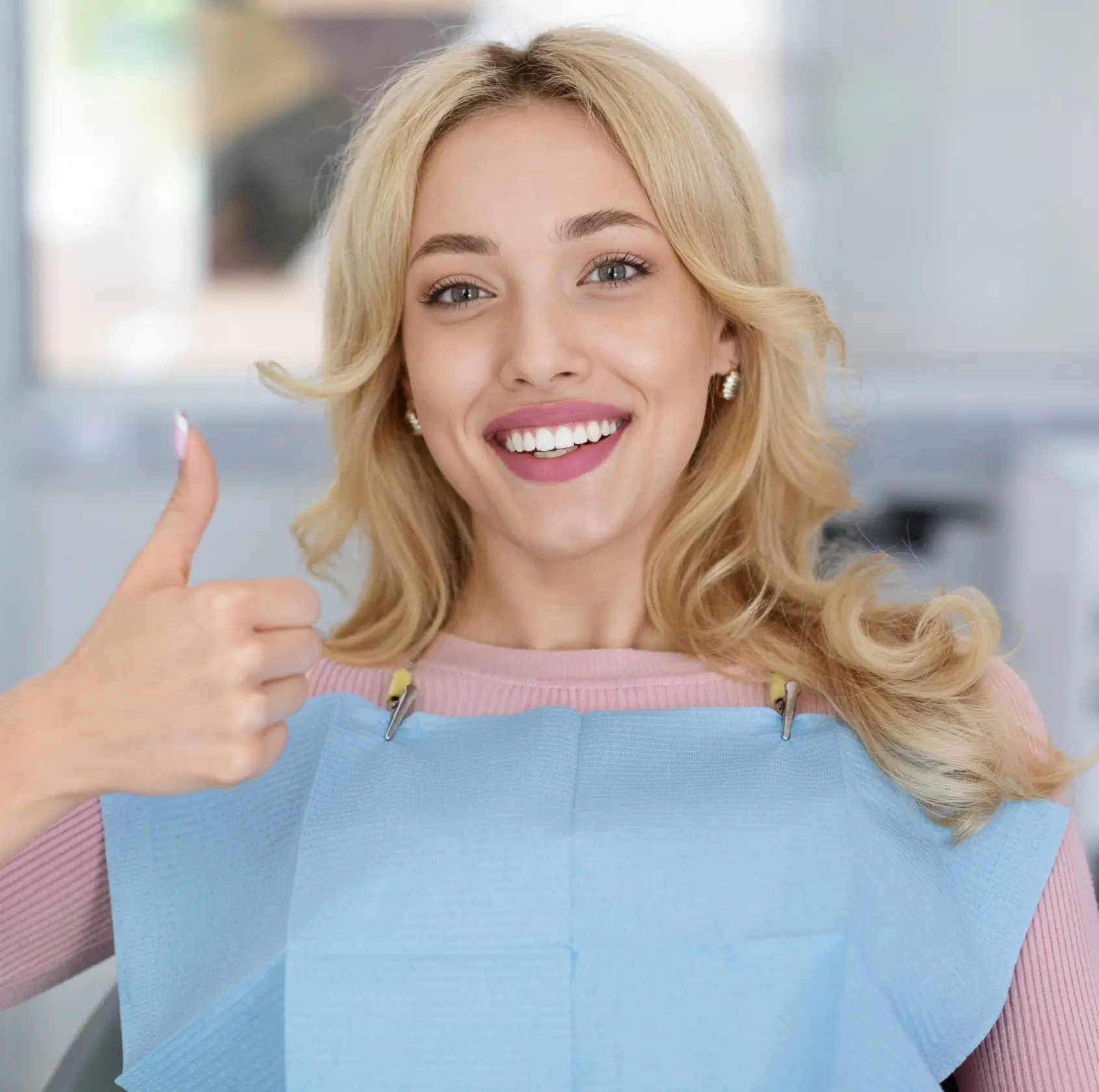 Smiling woman in dental bib giving thumbs-up during a dental checkup. La Perle Dental Center in Edmonton, AB TST 3T9