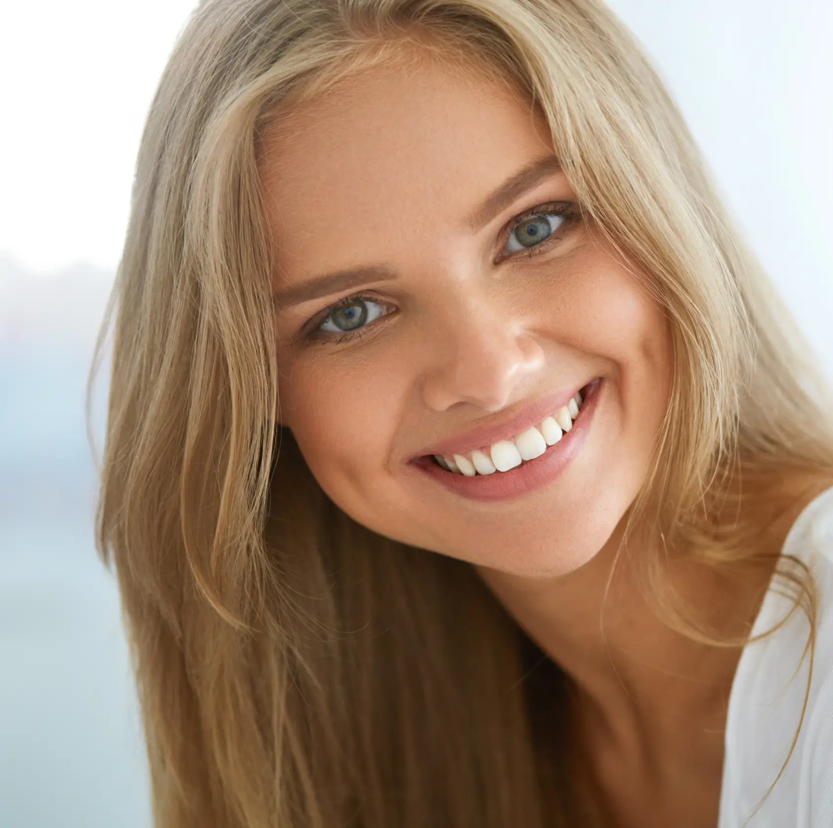 Close-up of a young woman with blonde hair smiling, showing bright white teeth. La Perle Dental Center in Edmonton, AB TST 3T9