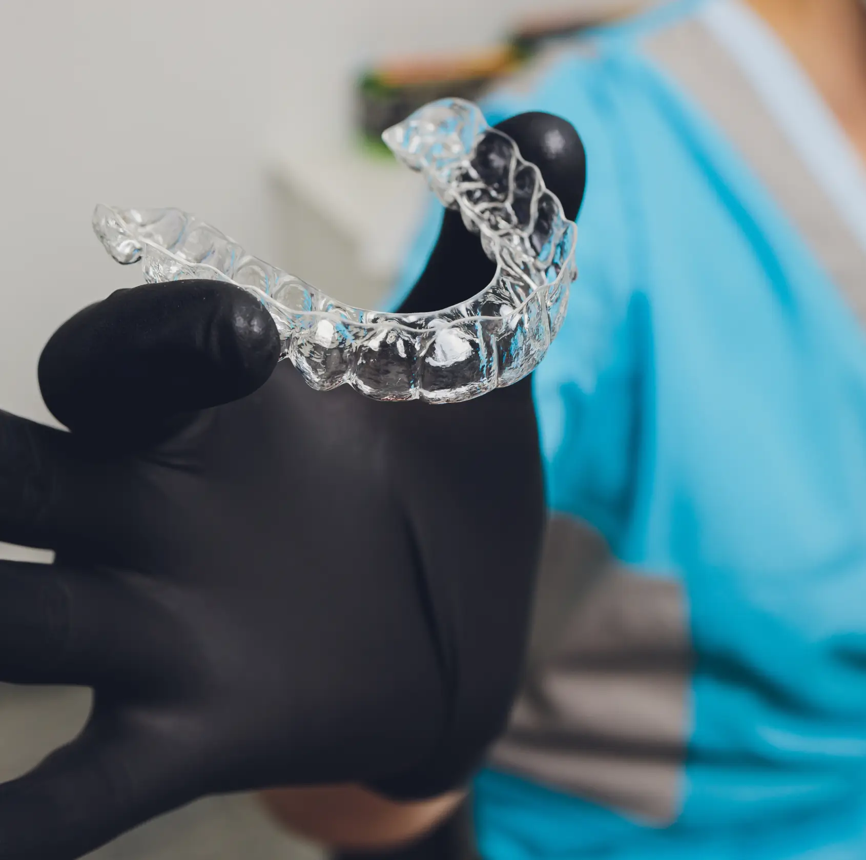 Gloved hand holding a clear dental aligner used for teeth straightening. La Perle Dental Center in Edmonton, AB TST 3T9