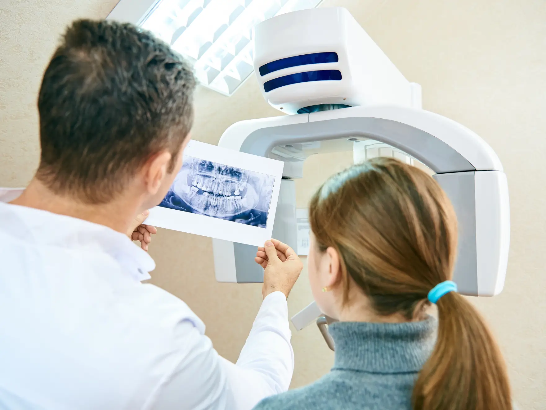 Dentist showing patient a dental X-ray image near a panoramic dental X-ray machine. La Perle Dental Center in Edmonton, AB TST 3T9