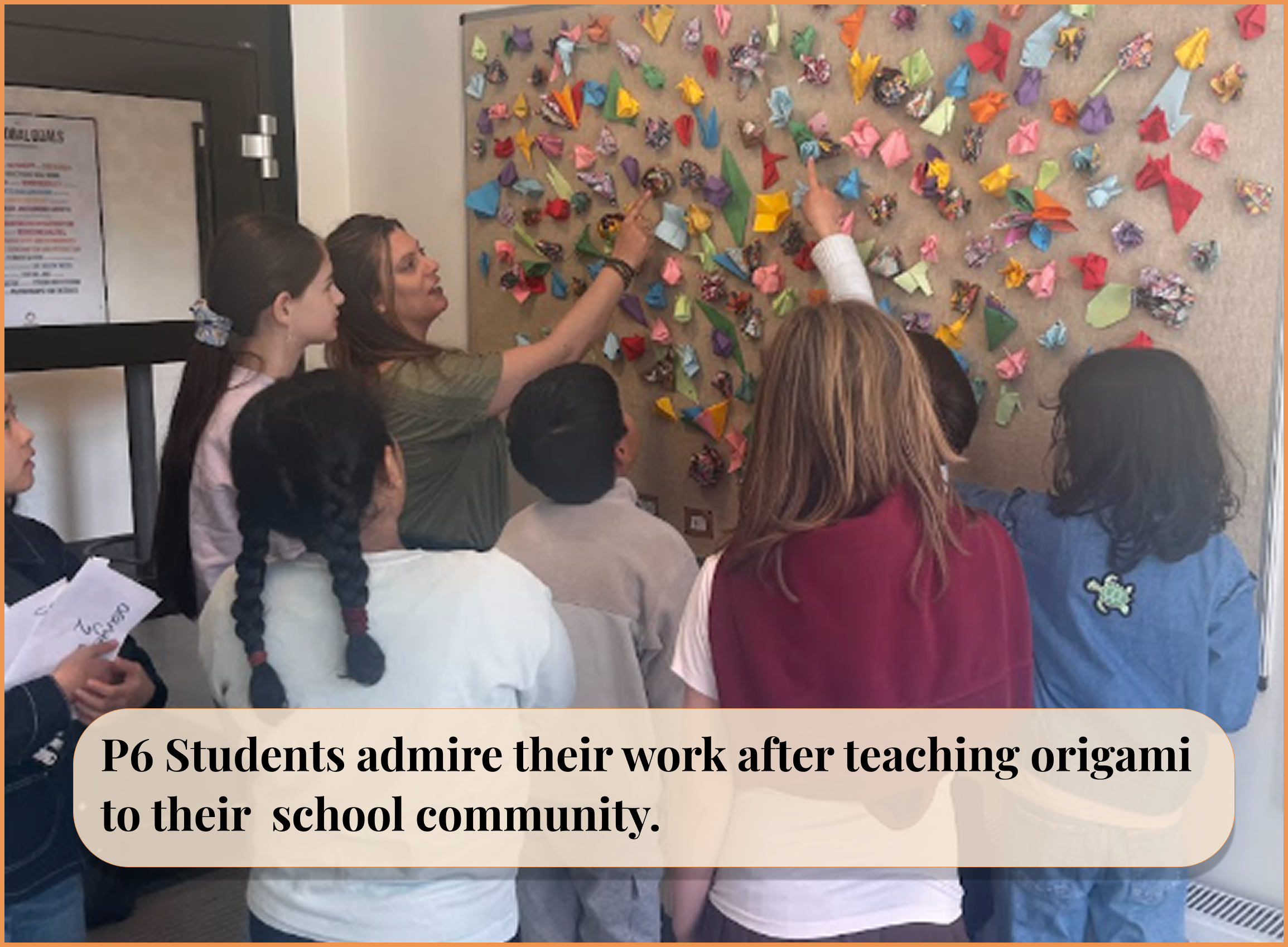 Group of seven children and an adult woman standing in front of a bulletin board decorated with various colorful origami pieces, admiring their paper crafts together.