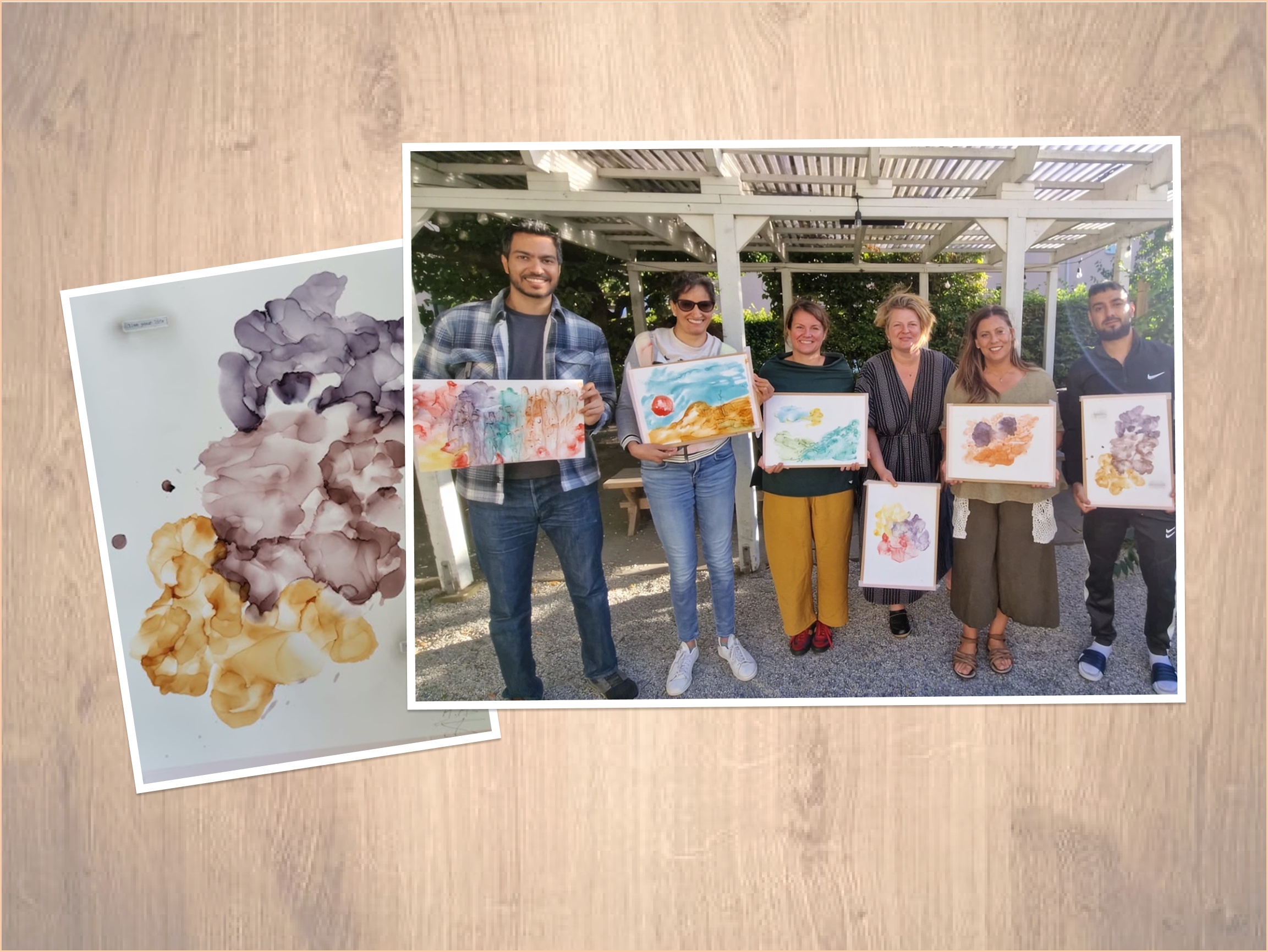Six people standing outdoors under a white pergola, each holding a colorful abstract watercolor painting, all smiling at the camera.