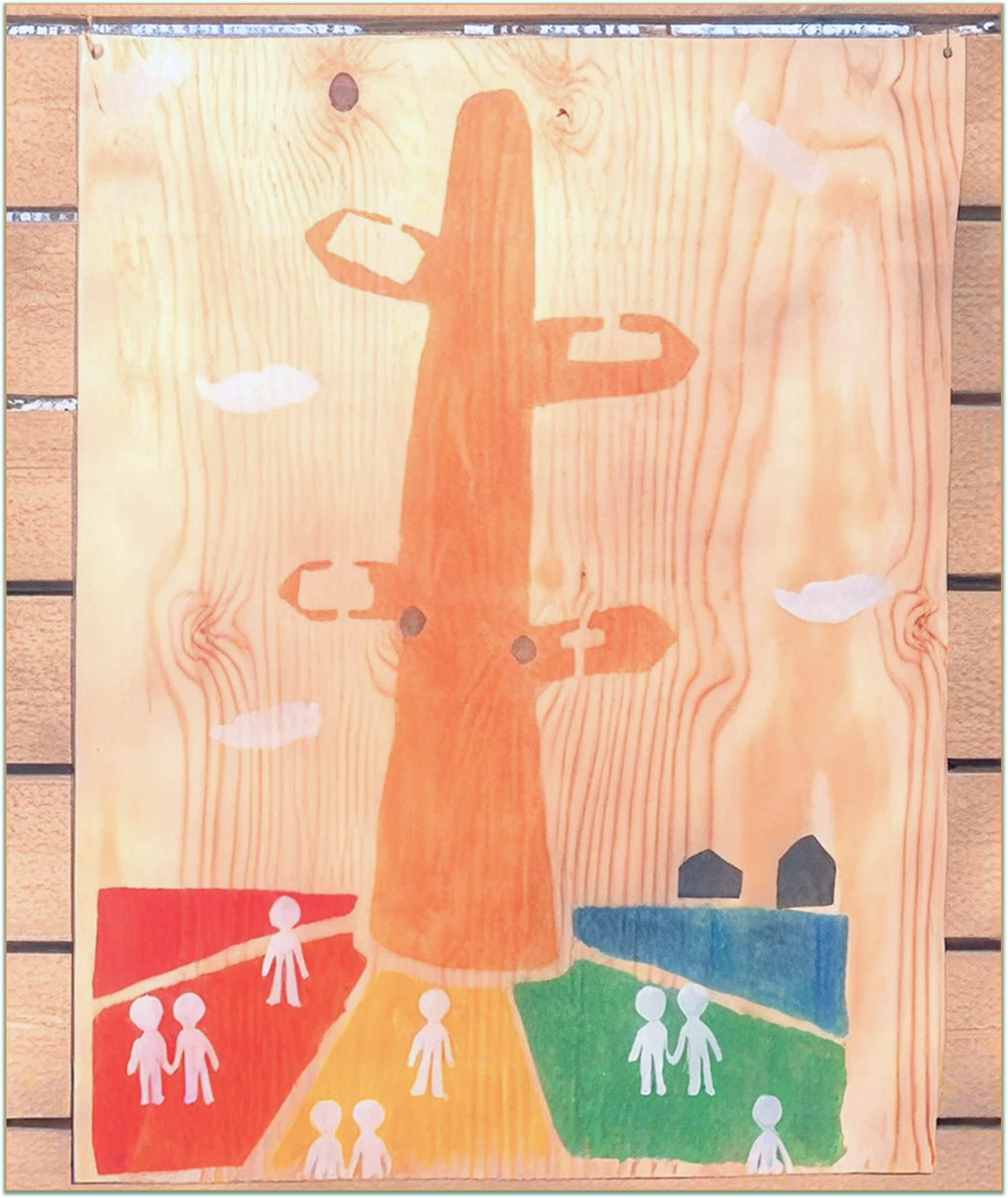 Wood panel painting featuring a large orange cactus in the center surrounded by four colorful sections on the bottom in red, yellow, green, and blue, each containing simple white human figures, with small blue house shapes on the blue section and white clouds in the background.