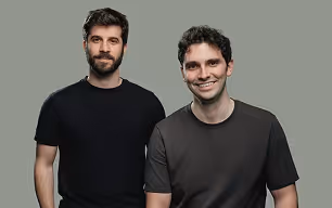 Deux hommes souriants portant des t-shirts noirs posant devant un fond gris.
