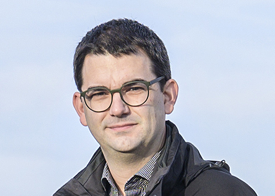 Michael Hoekstra mit runder Brille und dunkler Jacke vor hellem Himmel leicht zur Seite gedreht und in die Kamera blickend.