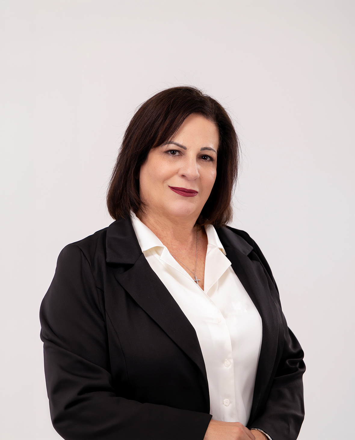 Confident woman with dark hair wearing a black blazer and white blouse against a white background.
