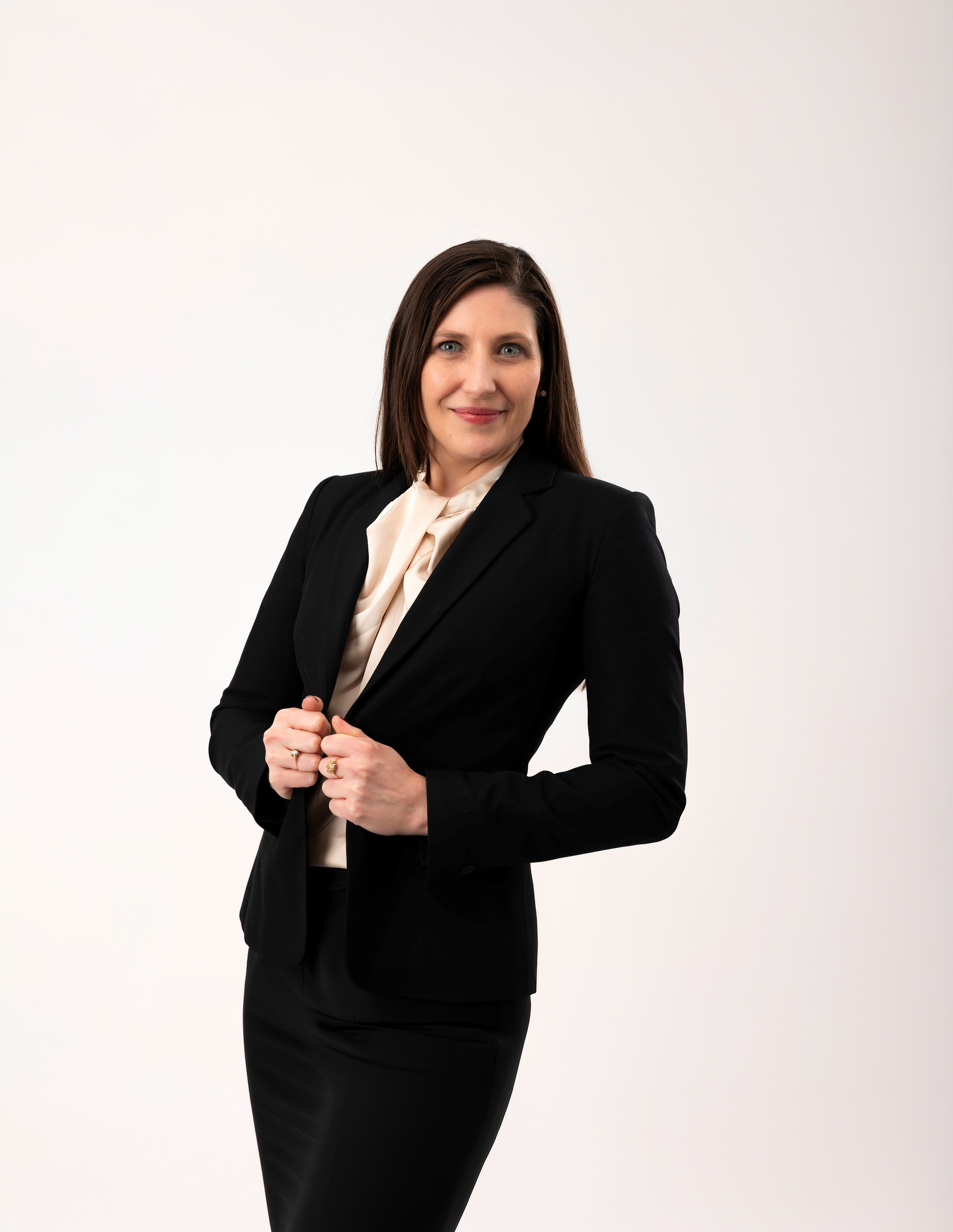 Professional woman in black suit jacket and skirt with cream blouse smiling against white background.