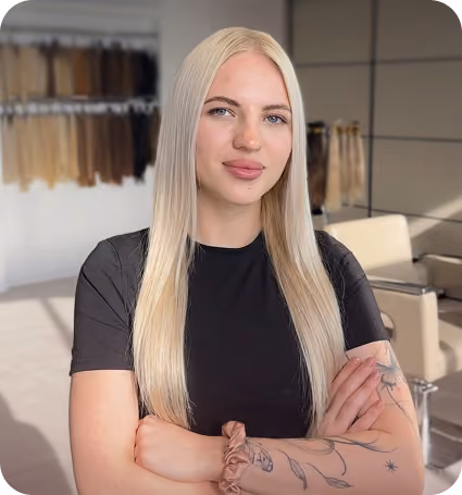 Kobieta z długimi, prostymi blond włosami w czarnej koszulce z tatuażami na przedramionach.