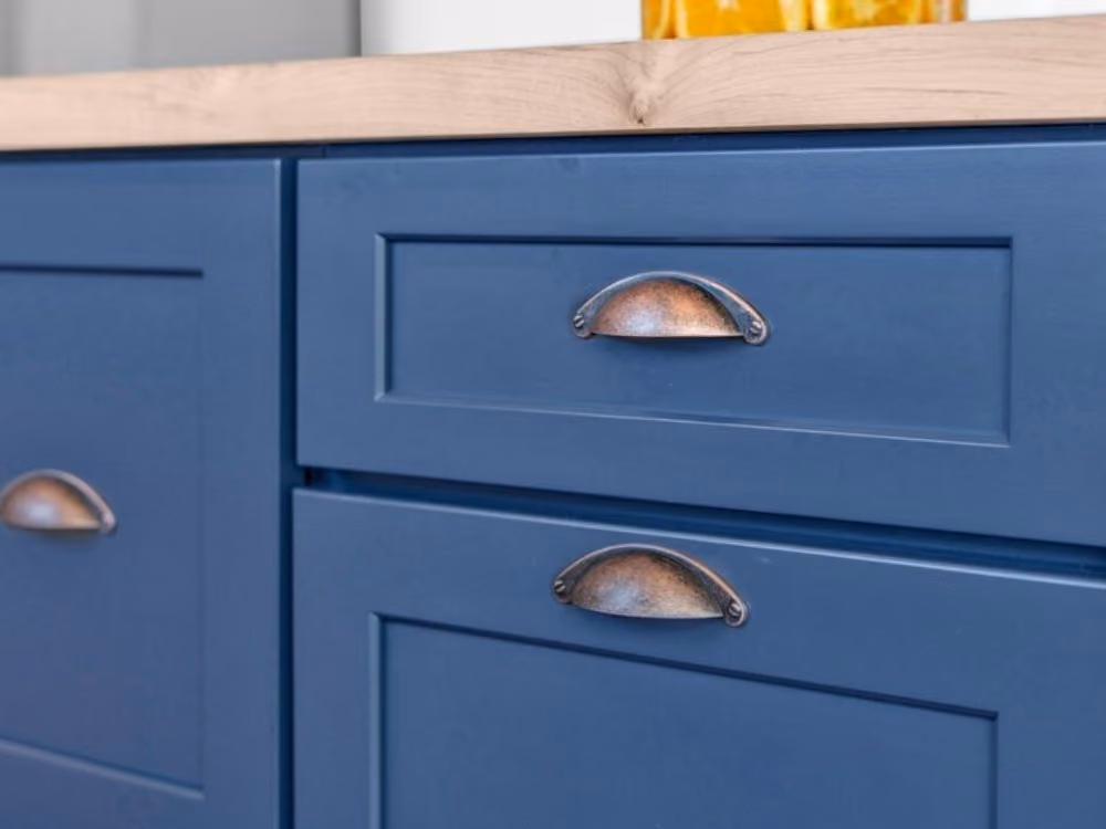 Close-up of blue kitchen cabinet doors and drawers with rustic half-moon metal handles and a light wood countertop.