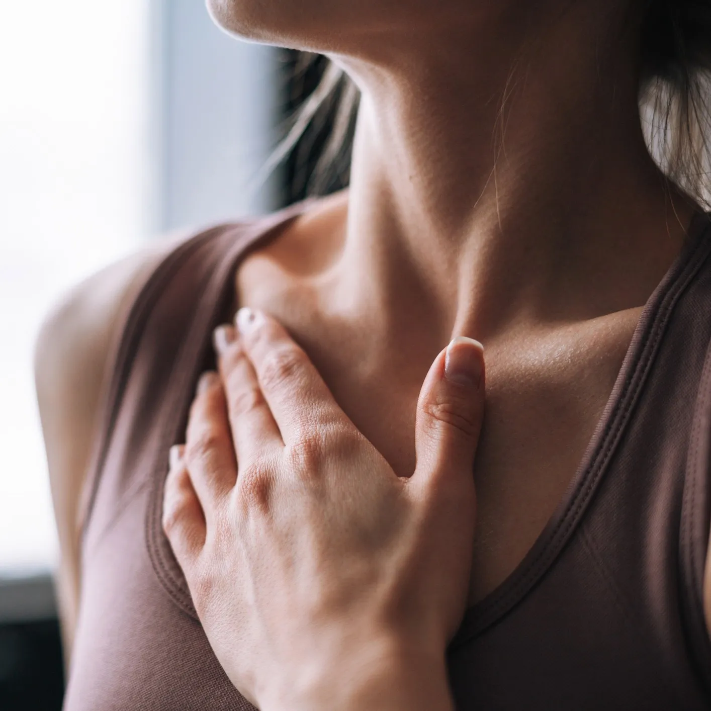 Close-up of a person wearing a sleeveless top with their hand placed gently on their chest near the collarbone.