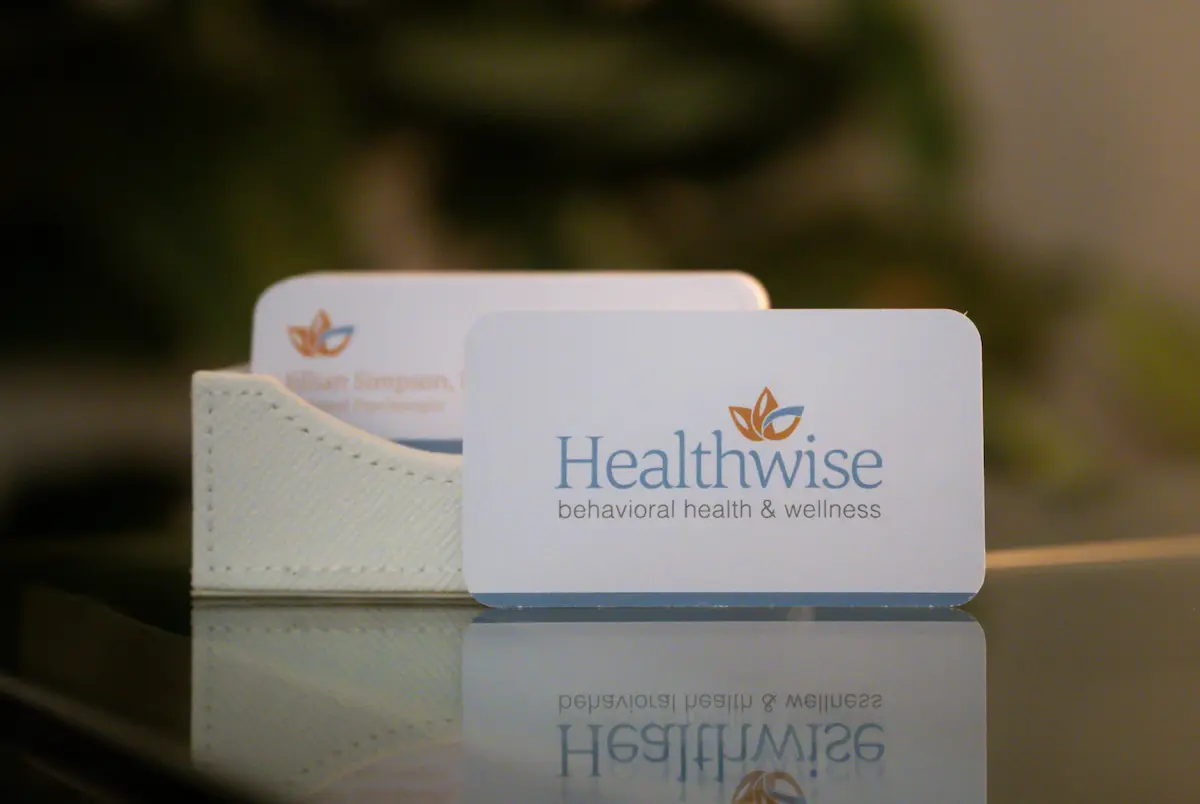 Close-up of a white business card holder with a card in front showing the logo and text 'Healthwise behavioral health & wellness' on a reflective surface.