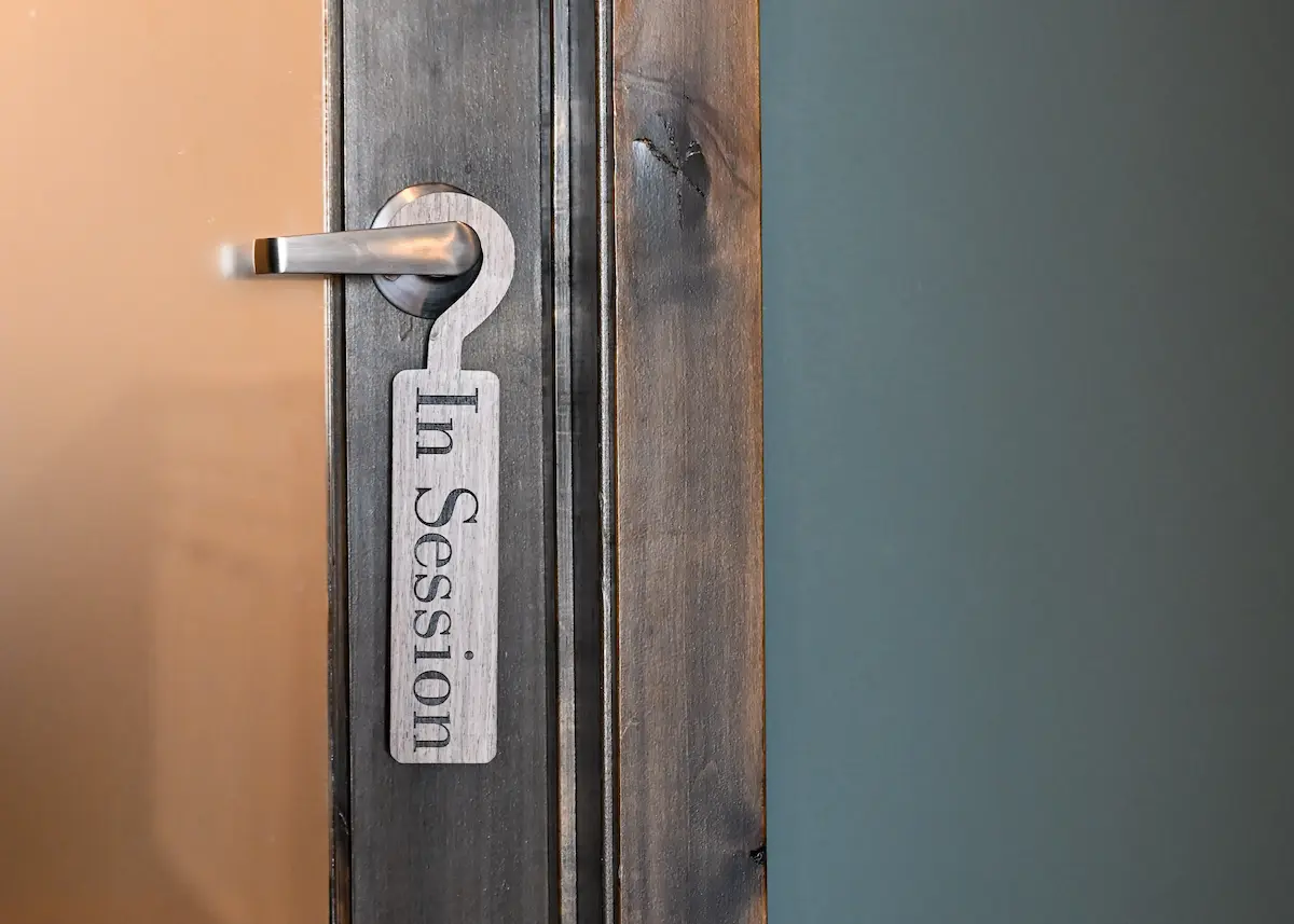 Wooden door with a metal handle and a hanging door sign that reads 'In Session'.