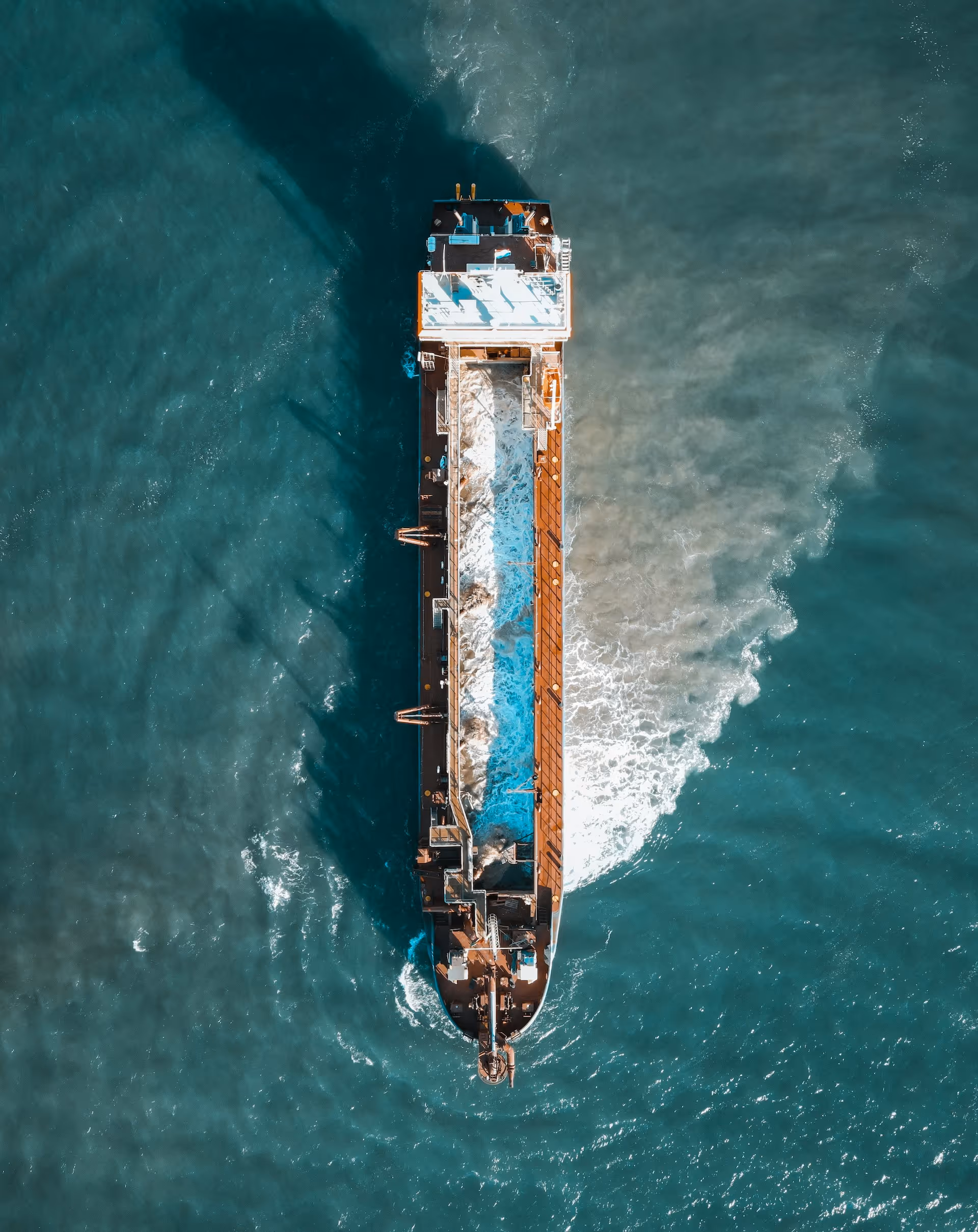 Aerial view of a cargo ship underway, leaving a white wake in turquoise water