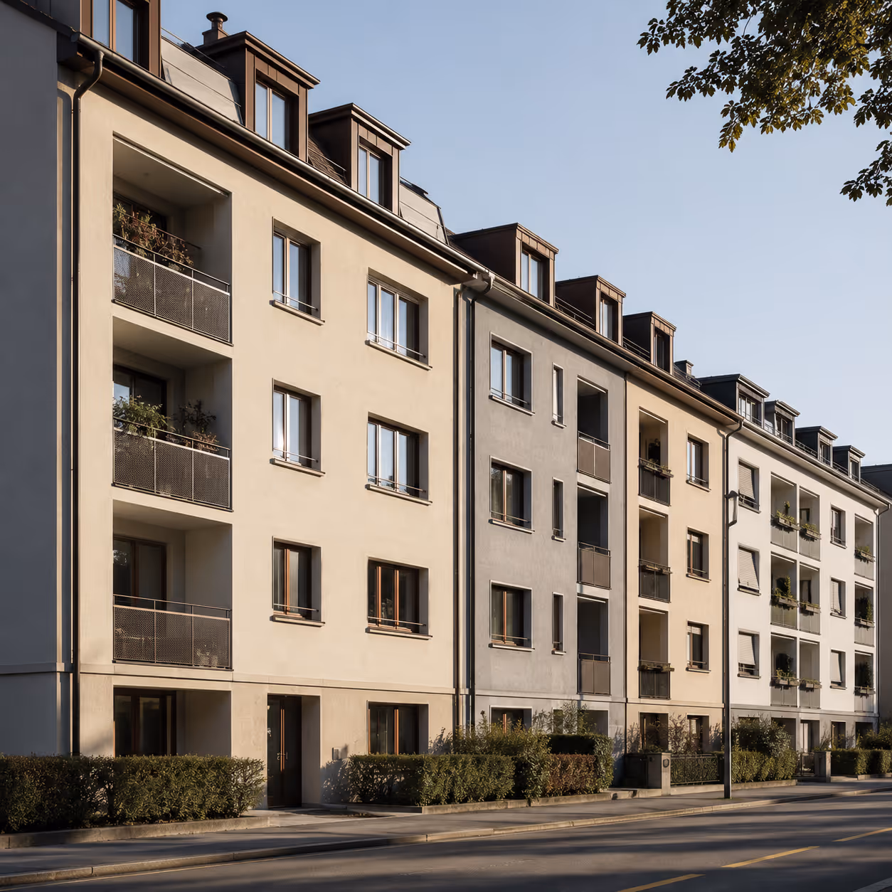 Reihe moderner Mehrfamilienhäuser mit Balkonen an einer ruhigen Straße bei sonnigem Himmel.