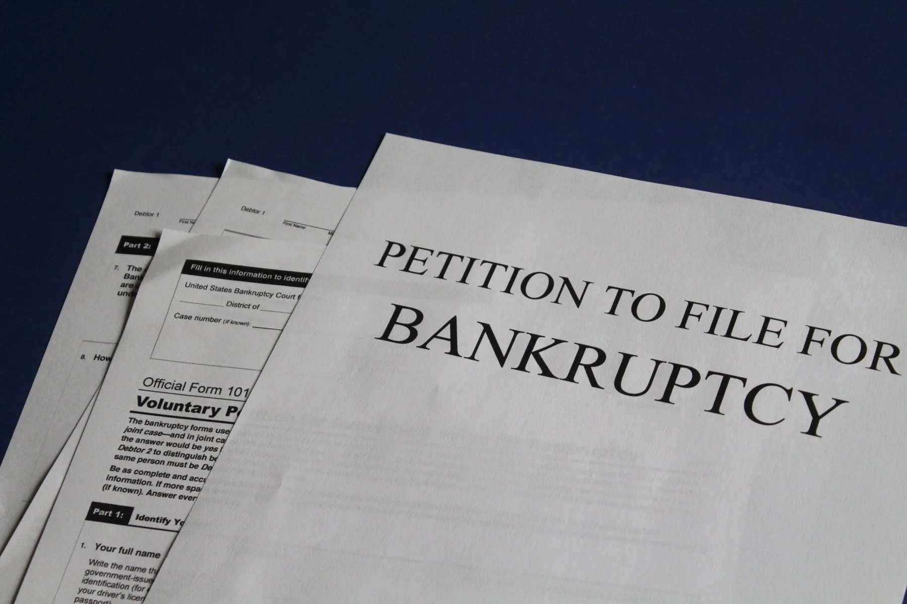 Stack of legal documents including a petition to file for bankruptcy on a dark blue surface.