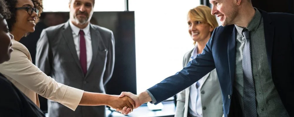 Businesspeople smiling and shaking hands in an office setting during a meeting.